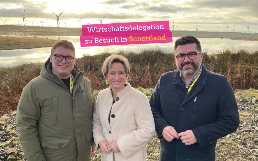 Drei Menschen stehen lächelnd nebeneinander. Landtagsabgeordneter Herkens (Grüne) Wirtschaftsministerin Hoffmeister-Kraut (CDU) und Landtagsabgeordneter Reith (FDP) vor dem größten OnShore Windpark in Schottland.